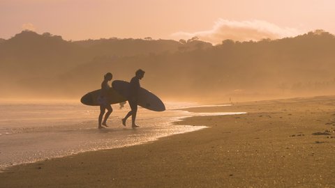 SLOW MOTION: Couple of surfers coming out of water after sunset surf session. Two friends after surf session in golden light at Playa Venao surf spot. Beach lifestyle shot in gorgeous light.: film stockowy