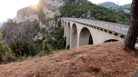 SLOW MOTION SHOT - The White Arc Bridge on Moyenne Corniche, cars, and motorcycles driving the road, Eze, Cote d'Azur, France. The Viaduct of Eze, The Bridge of the Devil, near Nice.
