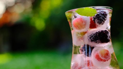 Berry cocktail.Splashes and drops of a Summer drink.Cocktail with gooseberries and blackberries, mint and ice cubes in a glass transparent glass in a summer garden in the sun.