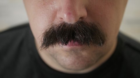 A man shaving off his thick black bushy mustache with an electric razor. Close up.