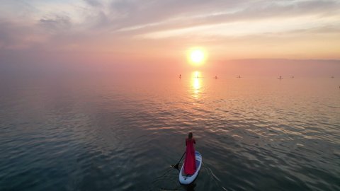 Sunset on Lake Baikal in summer. A girl in a red dress is floating on a sap board.
