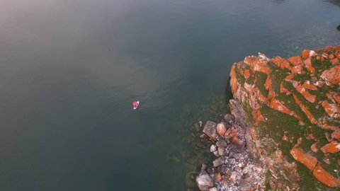 Top view of Shamanka Rock or Cape Burkhan at sunset. Lake Baikal in summer. A girl in a red dress swims on a sap board.