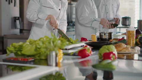 Portrait of female chef preparing celery ingredients for food dish, looking at camera. Woman in white uniform cooking professional meal with organic natural greens and salad for culinary recipe.