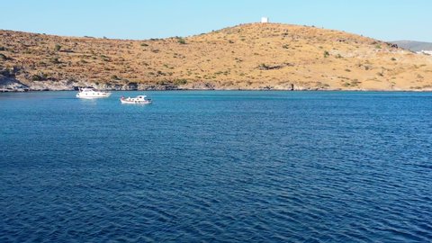 aerial drone circling two boats anchored in the bay near Bodrum Turkey during sunset enjoying the sunny summer afternoon with large hills in the background.