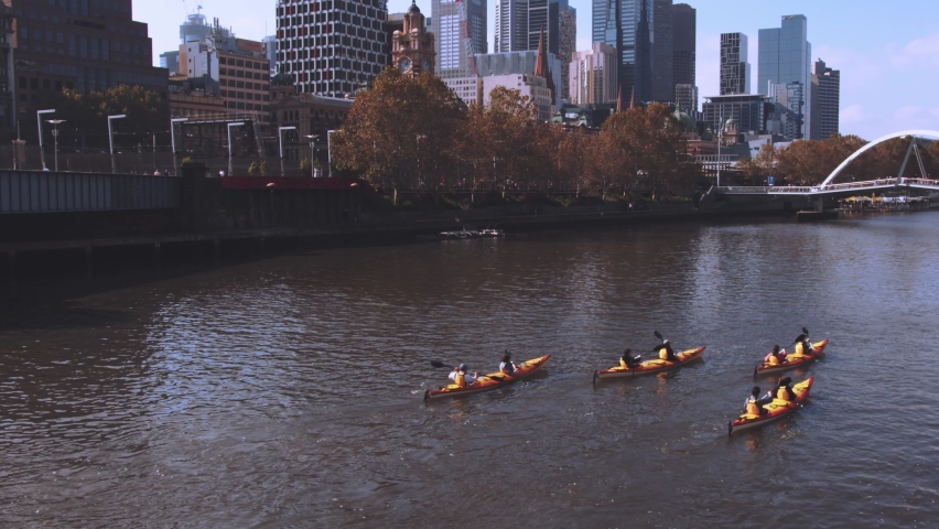 A group of four kayaks paddling up the Yarra River in Melbourne towards the Evan Walker Bridge, enjoying the views of the Southbank precinct