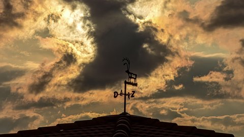 Low angle shot of house roof in rural village concept. View of vintage vane installed on the roof of a house to indicate wind direction with dark cloud movement over the evening sky.