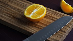 Man slicing raw orange with kitchen knife on wooden cutting board. Home cooking concept. Close-up