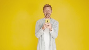 Young hispanic american man having fun using mobile phone watching funny videos over isolated yellow background