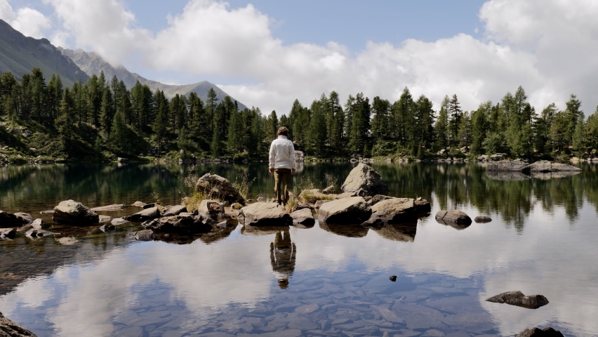 Man hiker admiring stunning Alpine lake, arms wide open 