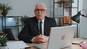 Senior business man ceo director sitting at workplace desk in office, looking at camera and having interview job discussion, video conference call. Elderly mature grandfather working at home office