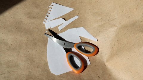4k video, Scissors with an orange handle lying on a cut white paper against a brown kraft sheet, rotation, top view
