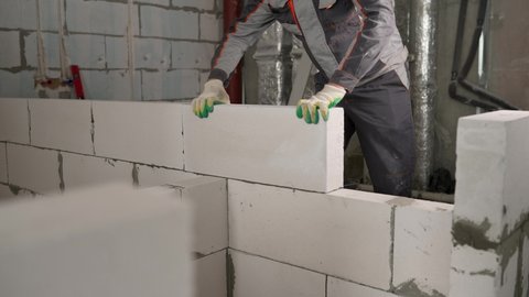 Construction site of a house made of light bricks. The master builds a wall of concrete blocks. Workers put blocks of bricks, construction work. The builder places a block when building a wall.
