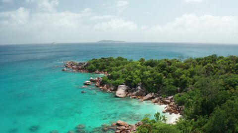 Aerial dolly over green cape of the coast bay Baie Chevalier with granite boulders, Petite Anse Lazio beach and blue emerald water toward to open Indian ocean and islands Booby and Aride, Praslin