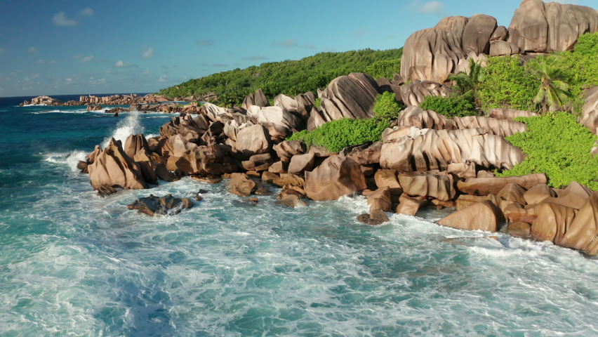 Aerial dolly over Anse Songe beach with raging Indian ocean fly very close over pink granite jagged rocks and huge boulders overlooking Grand l