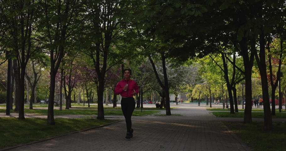 Pretty sporty woman jogging in the summer park with earphones listening to music, slow motion