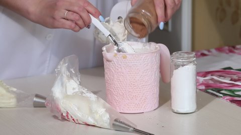 A woman adds cocoa to the cream for eclairs. Next to the jars are powdered sugar and cocoa powder. Medium plan
