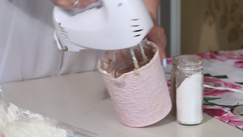 A woman adds cocoa to the cream for eclairs. Stirs with a mixer. Next to the jars are powdered sugar and cocoa powder. Medium plan.