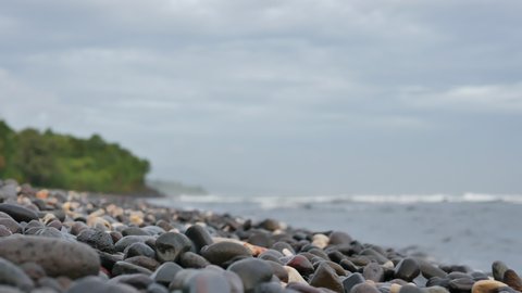 AMED, BALI, INDONESIA - JANUARY 30, 2018: Pebbled beach on sunrise and blurred oceanic waves in Amed, Bali. 4K, Shallow Depth of Field. Low angle, Audio