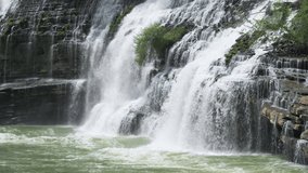 Stationary 4K video of waterfall cascading down a rocky cliff and then pouring into a green river full of rapids in Tennessee
