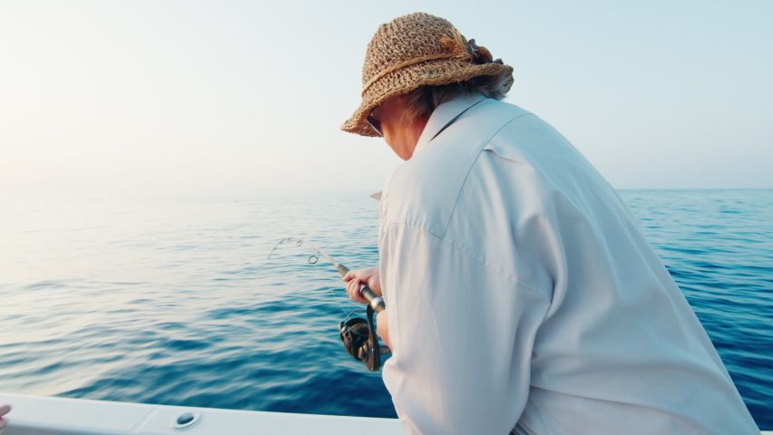 Family fishing trip in the open sea. Scared elderly woman holds fishing rod and pulls fish Royalty-Free Stock Footage #1089852029