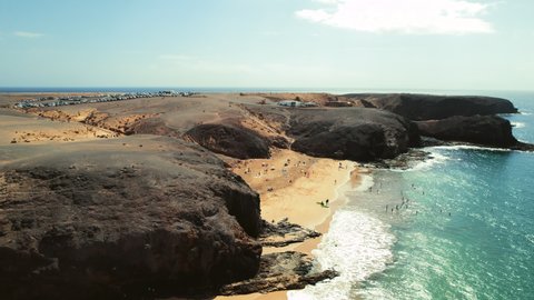 Drone point of view, aerial shot of sandy beach of Lanzarote. People relax on most popular Papagayo beach of Lanzarote, cove of white sand, Atlantic Ocean bay, crystal clear, green water. Spain