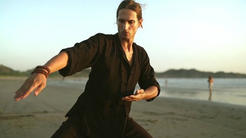 Healthy man exercising on beach, practicing qi gong, tai chi yoga. social distancing outdoor activity during isolation quarantine lockdown.