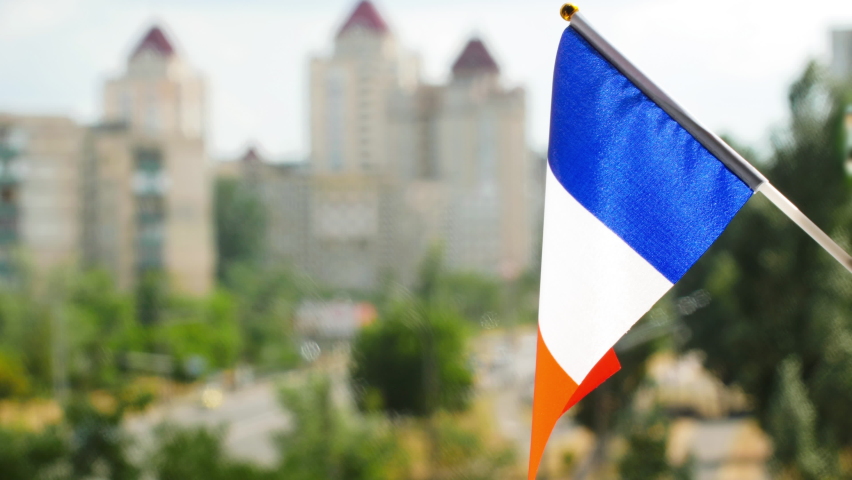 The national flag of France set against blue sky and city street. Tricolor French flag a vertical bands colored blue, white, and red flag. The holiday flag of the France waving. Copy space for text Royalty-Free Stock Footage #1089856257