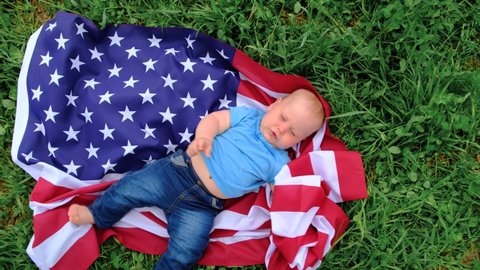 Excited baby lying on national USA flag outdoors over summer green grass - american flag, country, patriotism, independence memorial day 4th July.