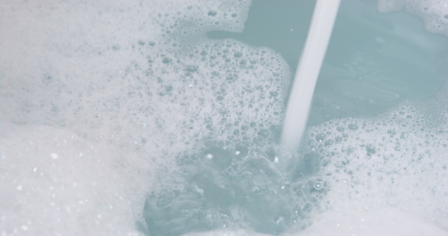 Bathroom with white bathtub full of warm water with thick layer of aromatic bubbles for relaxation. Preparation of taking bath at home or in hotel indoors. Spa, relaxation after a hard day