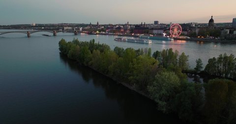 Sunset drone flight of Mainz over the Rhine river crossing a boat with a wine fest at the riverbank and summer evening sky in the back