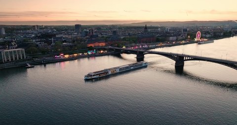 Sunset drone flight over Mainz at the Rhine river with a boat and the main city bridge in front of orange sky with a summer wine festival in the back