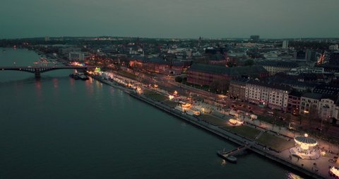 Drone aerial shot of Mainz pulling back from a wine festival showing the whole city in a wide shot over the Rhine river at a summer sunset with lots of city lights