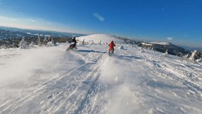 A sunlight aerial top view in mountains, two guy on snowmobile jumps and rides in the winter. Beautiful landscape