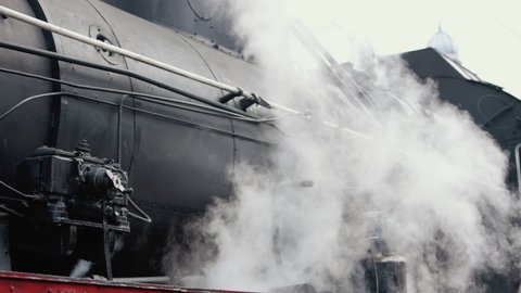 Smoke covering the train. Retro steam locomotive departs from the railway station. Old black steam train much smoke. Vintage locomotive with historical tour. Close-up