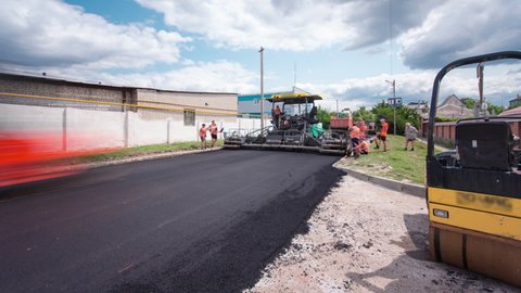 A paver finisher, asphalt finisher or paving machine placing a layer of asphalt during a repaving construction project timelapse. Steam rollers compacting