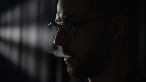 A face of a brutal bearded man smoking an electronic cigarette. Dark mysterious background with little smoke. Shot from the film. Man against a dark background