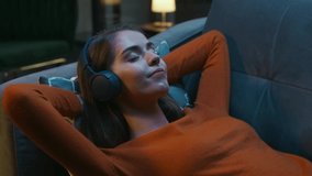 Young Woman is Lying at Home on the Couch with her Eyes Closed and Listening to Music on Headphones. Woman is Resting and Hearing to Online Radio. Relaxation, Meditation and Mindfulness. - Powered by Shutterstock - Get 15% off with code: PIKWIZARD15