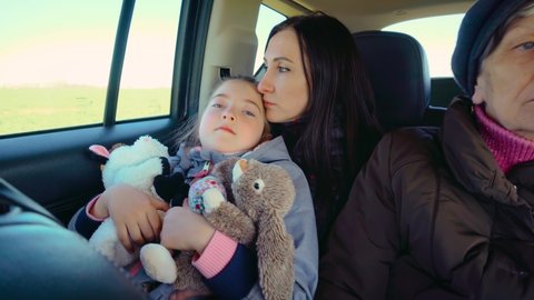 War refugees mother with her daughter and senior woman driving in back seat of car during evacuation from Ukraine. Concept of peaceful and carefree life without armed conflicts