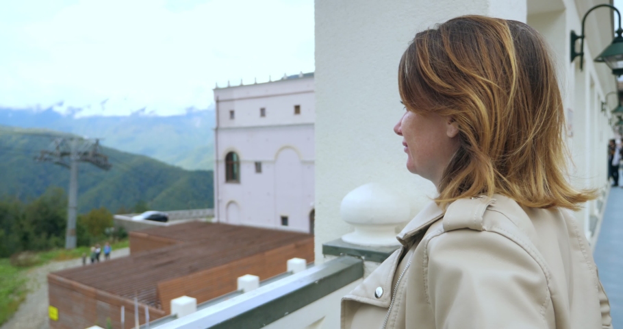 a woman in a white leather jacket is watching the movement of the funicular enjoying the scenery in a mountain resort.