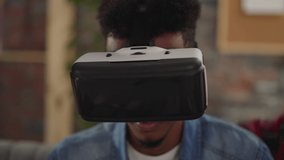 Bearded African-American guy with VR headset enjoys 3d movie effects sitting with friends in living room closeup slow motion. Technology of entertainment