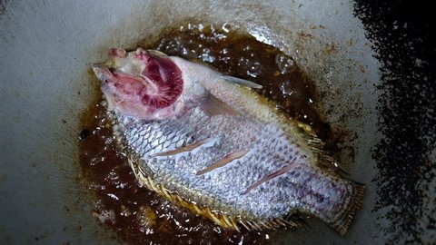 Frying Tilapia fish in a pan of oil.