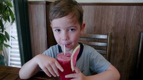Little boy drinking freshly squeezed watermelon juice. Portrait Funny little child drinks a cup of juice. Cute boy drinking a glass of watermelon juice while sitting in the kitchen at home.