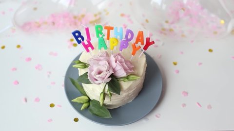 Young woman Lighting the Candles of a Cake in the form of a word - Happy Birthday, and puts out the match. Close up footage of white cream festive pie. Birthday Cake With Burning Colorful Candles