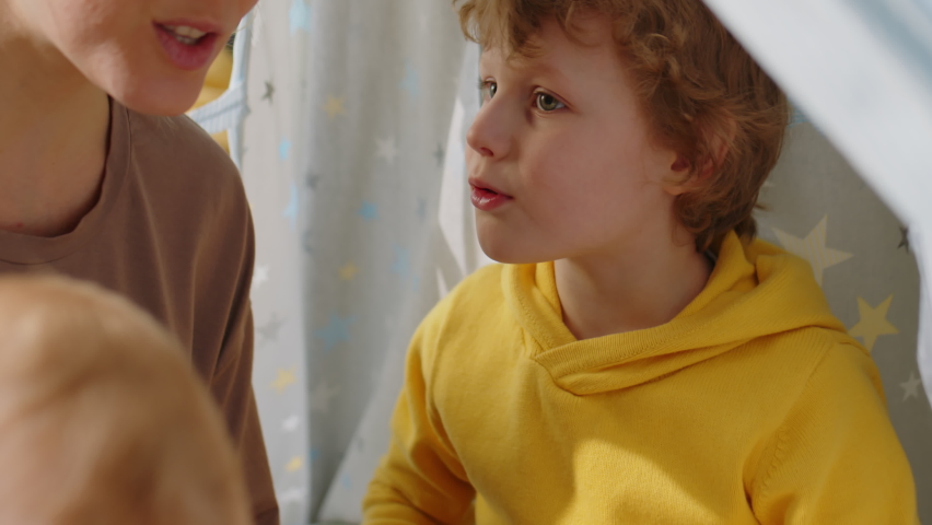 Mother speaking with little sons while playing together in teepee tent at home
