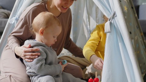 Mother sitting with baby boy and elder son in teepee tent at home as kids playing with developmental toy