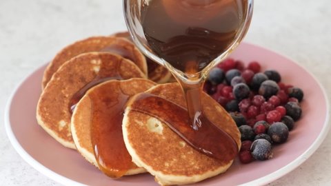Slow motion syrup pouring on pancakes served with berries. Sweet breakfast food