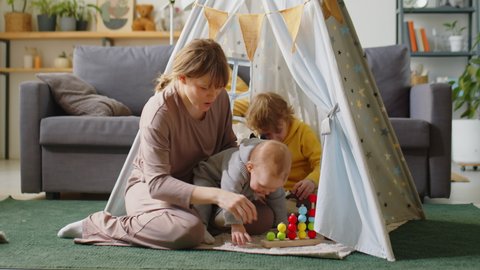 Mother and two little kids playing with developmental toy in teepee tent at home
