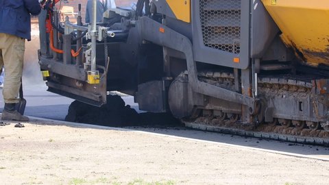 An asphalt paver is laying new asphalt on top of an old, road repair. Special road equipment, industry, close-up