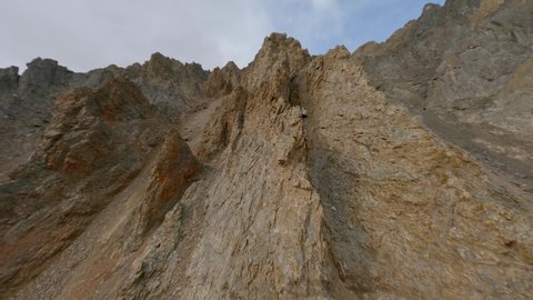 Aerial view flying over organic mountain summit cracked texture stone pebble cliff geology formation surrounded by snow. FPV sports drone shot volcanic canyon valley scenery wilderness ridge panorama