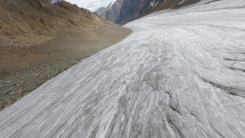 Cracked natural glacier snowy shaky texture at picturesque mountain valley. Aerial view dive low fast movement FPV sports drone view cliff snow summit adventure altitude organic wild environment fauna